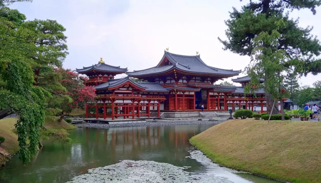 Templo Byodo-in em Kyoto, cercado por um lago com nenúfares e árvores floridas ao redor.