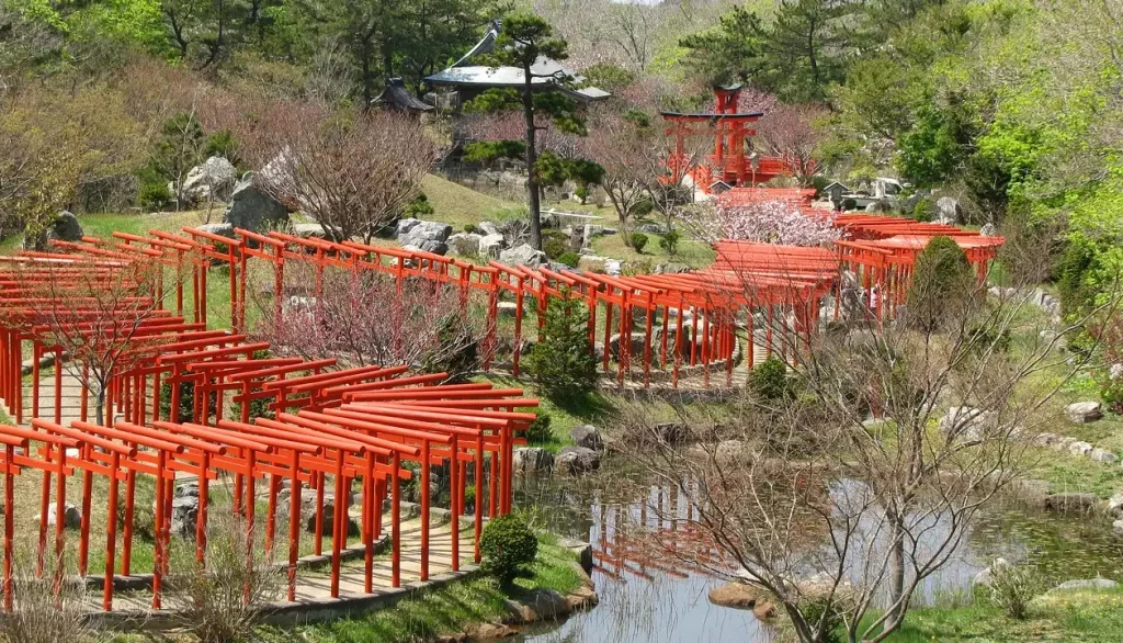 Caminho de portões torii vermelhos em Fushimi Inari, Kyoto, com vegetação ao redor e céu limpo.