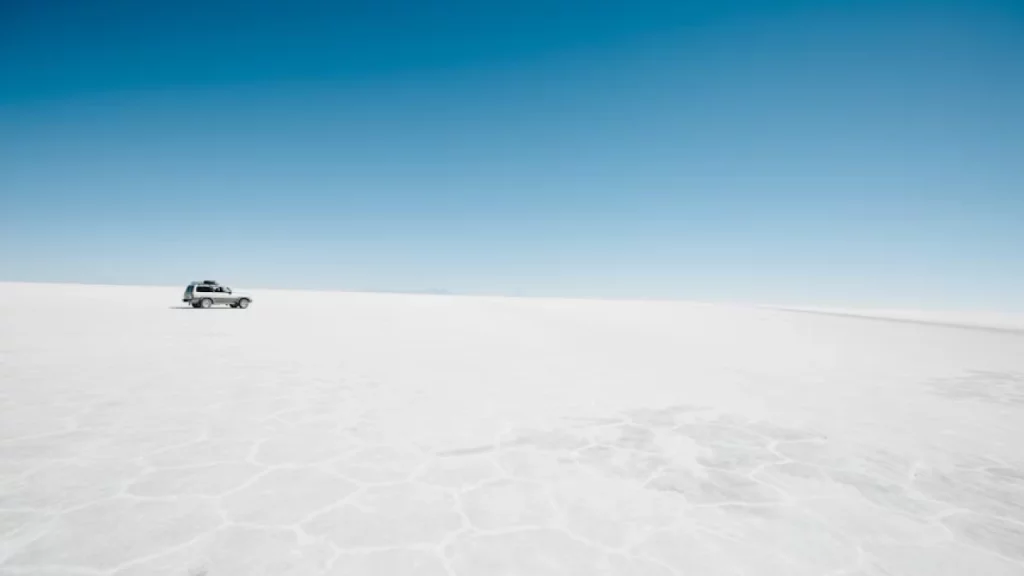 Veículo atravessando o vasto e deslumbrante Salar de Uyuni, o maior deserto de sal do mundo, na Bolívia, sob um céu azul claro