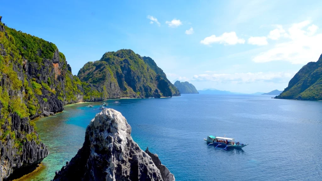 Vista panorâmica das águas cristalinas e formações rochosas imponentes em El Nido, Filipinas, com barcos tradicionais flutuando no mar