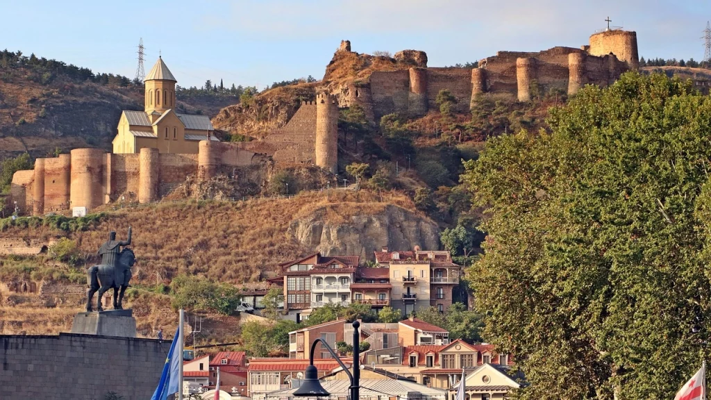 Antiga fortaleza Narikala e a Igreja de São Nicolau em Tbilisi, Geórgia, com arquitetura histórica cercada por colinas e vegetação exuberante