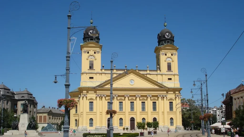 Fachada da Grande Igreja Reformada de Debrecen, Hungria, em um dia ensolarado, com céu azul e poucas pessoas na praça em frente