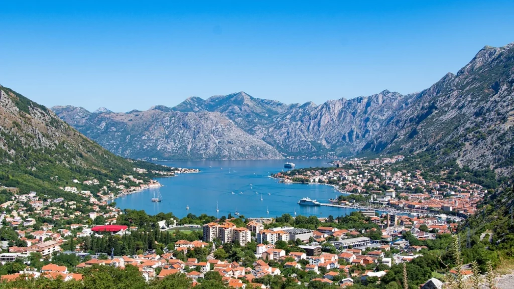 Vista aérea da Baía de Kotor, Montenegro, com montanhas ao fundo e telhados de terracota, revelando a beleza histórica e natural do local