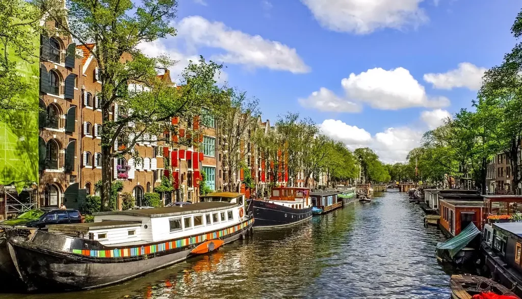 Vista de um canal em Amsterdã com barcos coloridos e prédios históricos alinhados ao longo da margem, destacando a charmosa arquitetura e os canais icônicos da cidade.