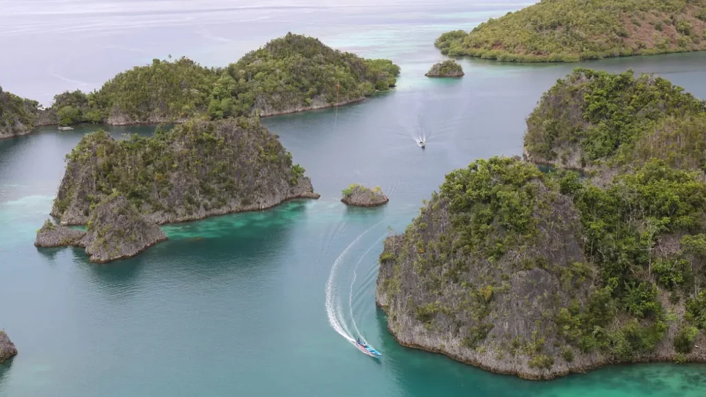 Uma vista aérea das ilhas de Raja Ampat, na Indonésia, com formações rochosas cobertas por vegetação exuberante e águas cristalinas de um verde vibrante, onde barcos deslizam suavemente.