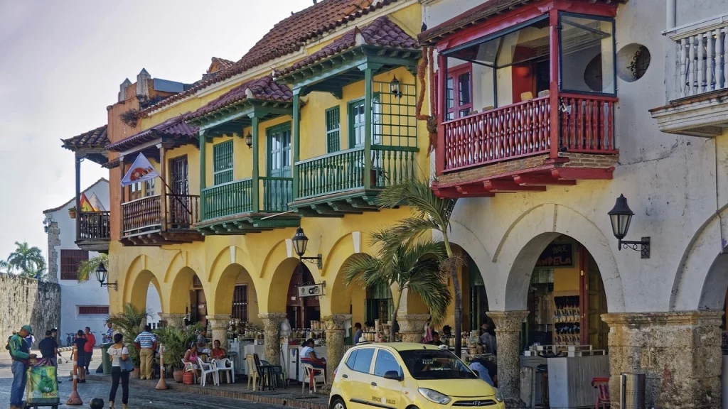 Ruas coloridas e charmosas de uma cidade histórica com casas coloniais, varandas de madeira e um carro amarelo estacionado em frente a um restaurante.