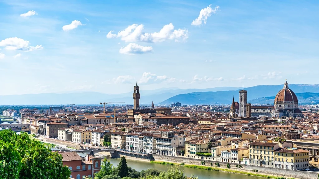 Panorama de Florença, com destaque para a cúpula da Catedral de Santa Maria del Fiore e os prédios históricos ao longo do rio Arno, em um dia ensolarado.