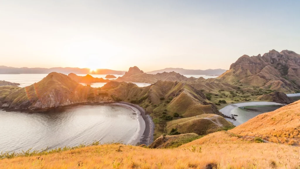  Pôr do sol em Komodo Island, Indonésia, com colinas douradas e baías tranquilas que refletem o brilho alaranjado do sol, criando uma vista deslumbrante.