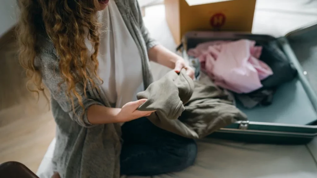 Mujer empacando ropa en una maleta, asegurándose de incluir tanto ropa de verano como ropa abrigada para un viaje.