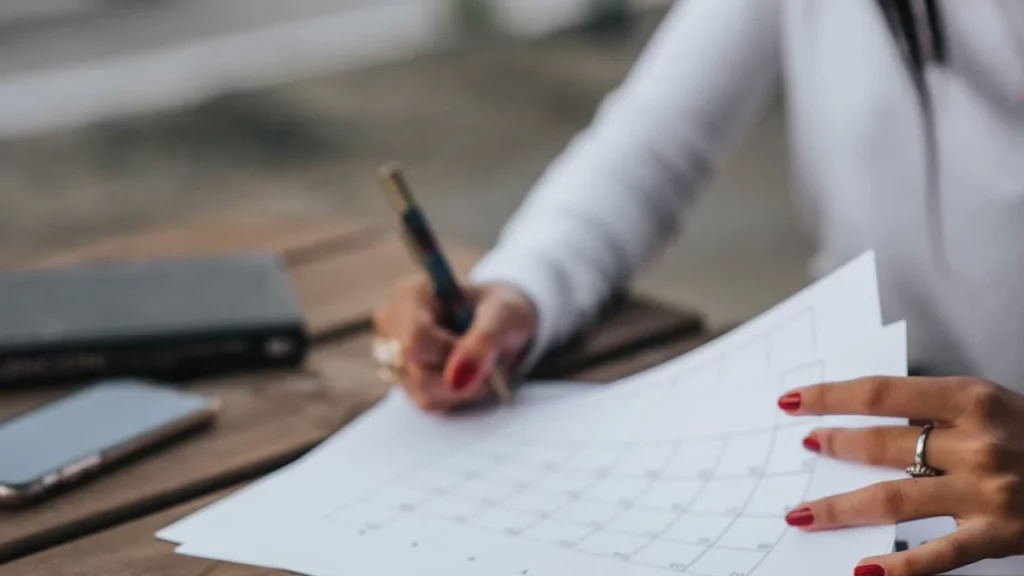 Mano de una persona escribiendo en un calendario de planificación de viajes, organizando fechas para evitar la temporada alta en Cancún.