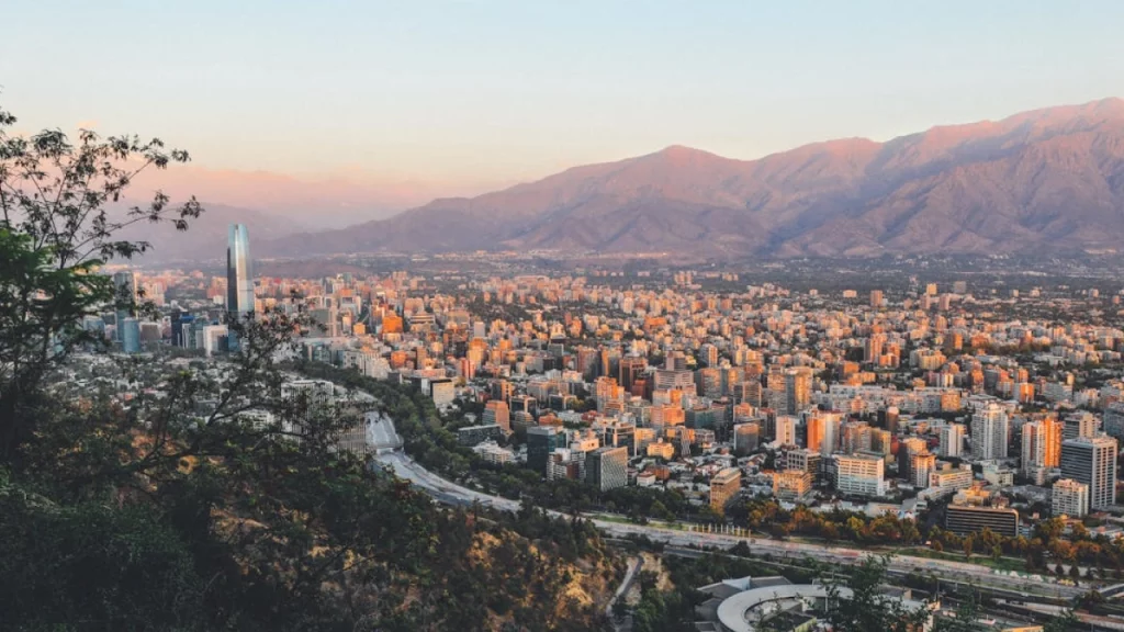 Vista panorâmica de Santiago ao pôr do sol, com a Cordilheira dos Andes ao fundo e a moderna skyline da capital chilena em destaque.