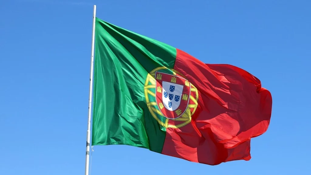 Bandeira de Portugal tremulando contra um céu azul claro.