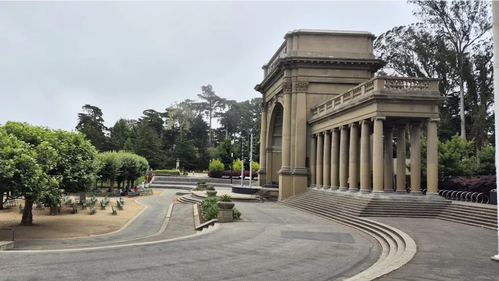 Praça Music Concourse no Golden Gate Park, San Francisco, em um dia nublado, com árvores ao redor e uma estrutura de colunatas ao fundo.