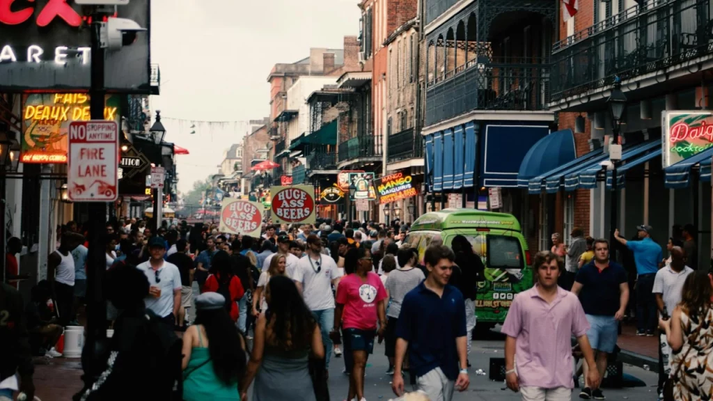 A animada Bourbon Street, em Nova Orleans, com uma multidão de pessoas explorando a rua repleta de bares e letreiros luminosos.