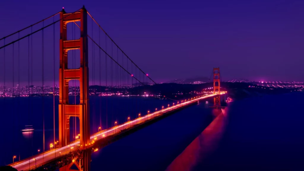 A icônica Ponte Golden Gate, em São Francisco, iluminada à noite, destacando-se contra o céu escuro e as luzes da cidade ao fundo.