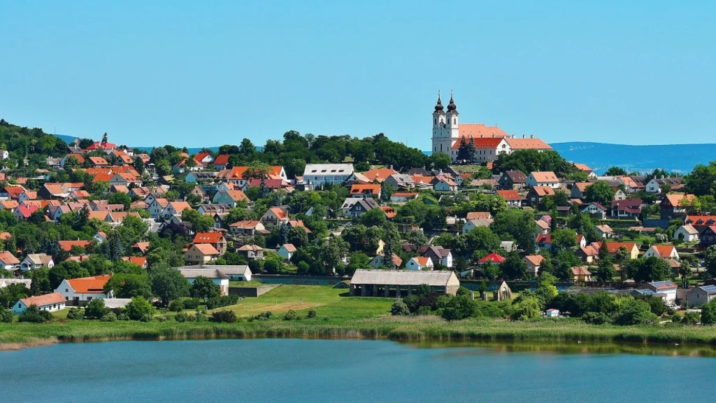 Vista da cidade de Tihany, Hungria, com casas coloridas e uma igreja no topo da colina, vista do lado oposto de um lago.