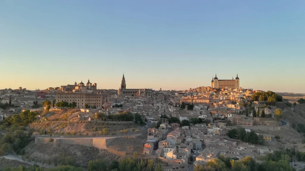 Vista panorâmica da cidade de Toledo ao anoitecer, com a catedral e o alcázar em destaque no horizonte.