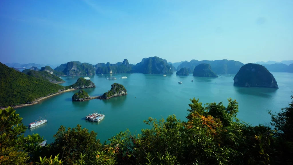 Vista panorâmica da Baía de Halong, no Vietnã, com várias ilhas de calcário emergindo das águas azuis e barcos flutuando pacificamente.