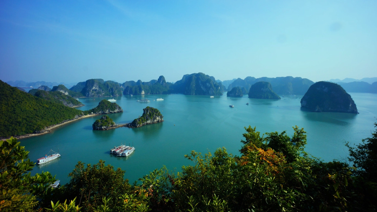 Vista panorâmica da Baía de Halong, no Vietnã, com várias ilhas de calcário emergindo das águas azuis e barcos flutuando pacificamente.