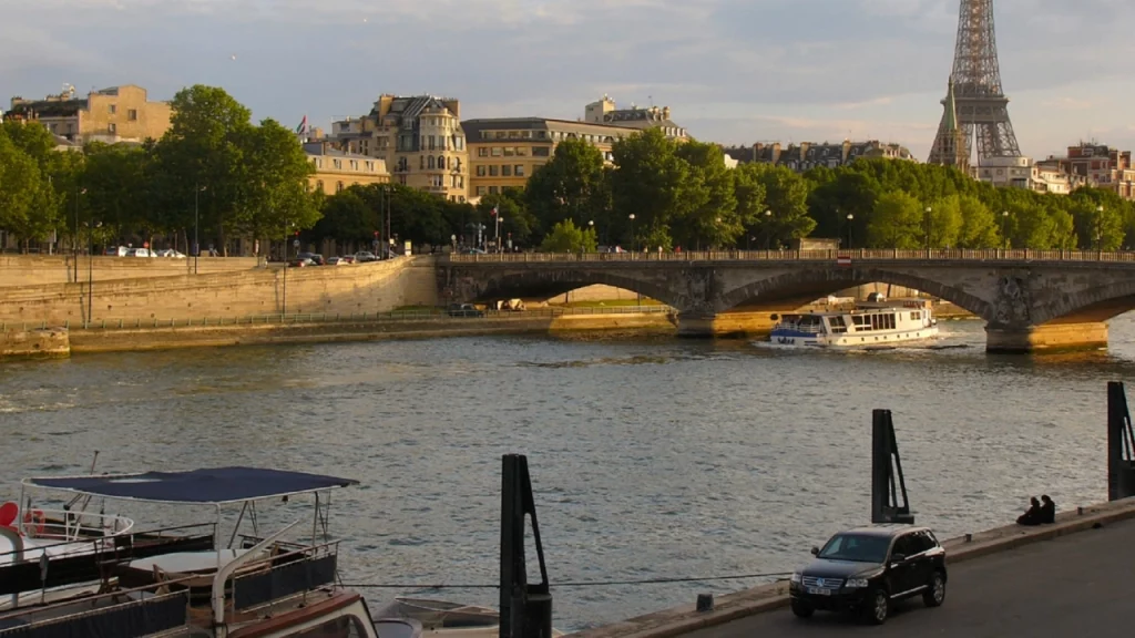 Vista do Rio Sena em Paris com a Torre Eiffel ao fundo, uma ponte antiga atravessando o rio e barcos navegando ao longo da água.