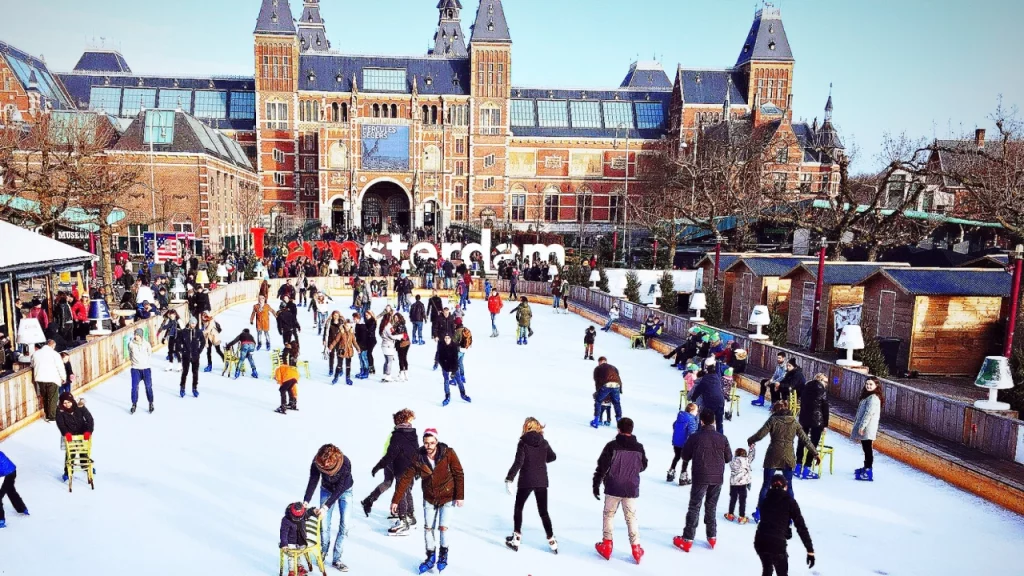 Pessoas patinando em uma pista de gelo em frente ao Museu Rijksmuseum em Amsterdã, em um ambiente de inverno festivo.