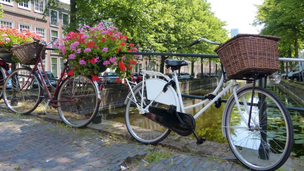 Bicicletas decoradas com cestas e flores coloridas estacionadas ao longo de um canal em Amsterdã, em um dia ensolarado.