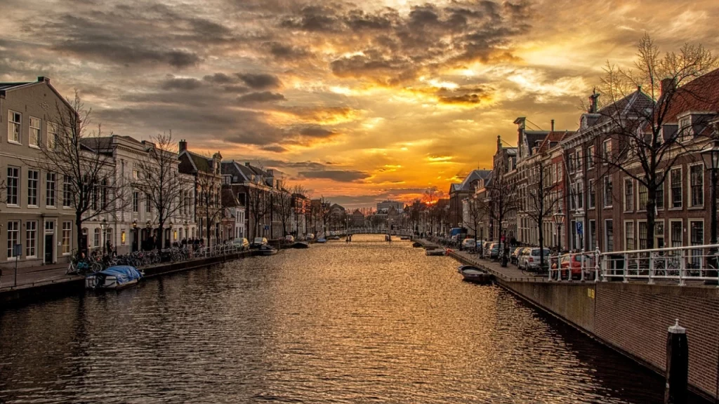 Pôr do sol em um canal na Holanda, com casas alinhadas e uma atmosfera tranquila, destacando a beleza das paisagens urbanas do país.