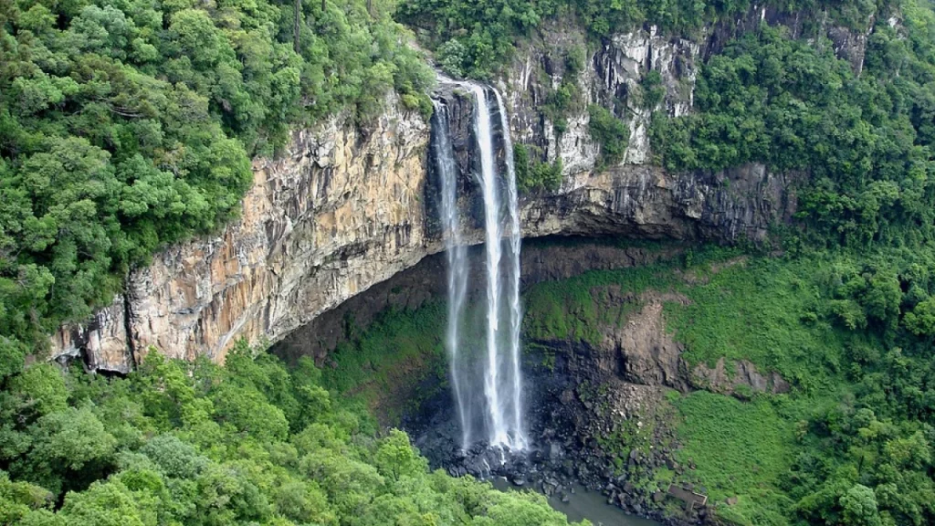 A imponente Cascata do Caracol em Canela, Rio Grande do Sul, cercada por uma exuberante vegetação verde e um paredão rochoso impressionante.