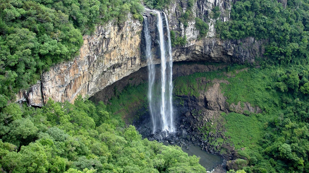 Vista aérea da Cascata do Caracol em Canela, RS, rodeada por uma densa vegetação verde e imponentes paredões de pedra.