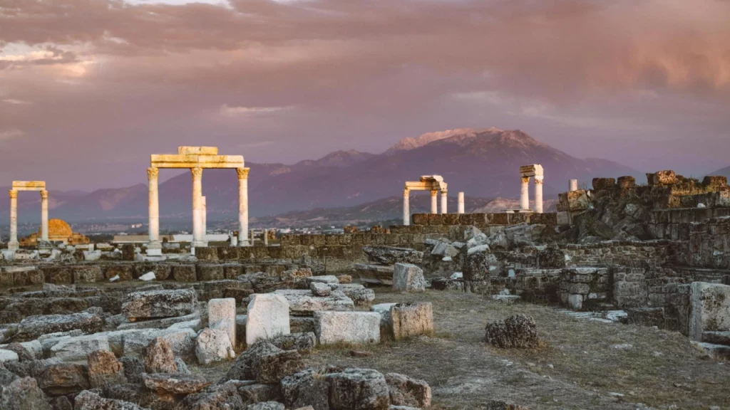 Ruínas da cidade de Laodiceia, na Turquia, com colunas antigas e montanhas ao fundo ao pôr do sol.