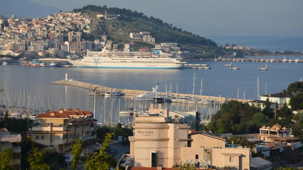 Kuşadası, na Turquia, com um grande cruzeiro atracado no porto e vista das colinas com casas.