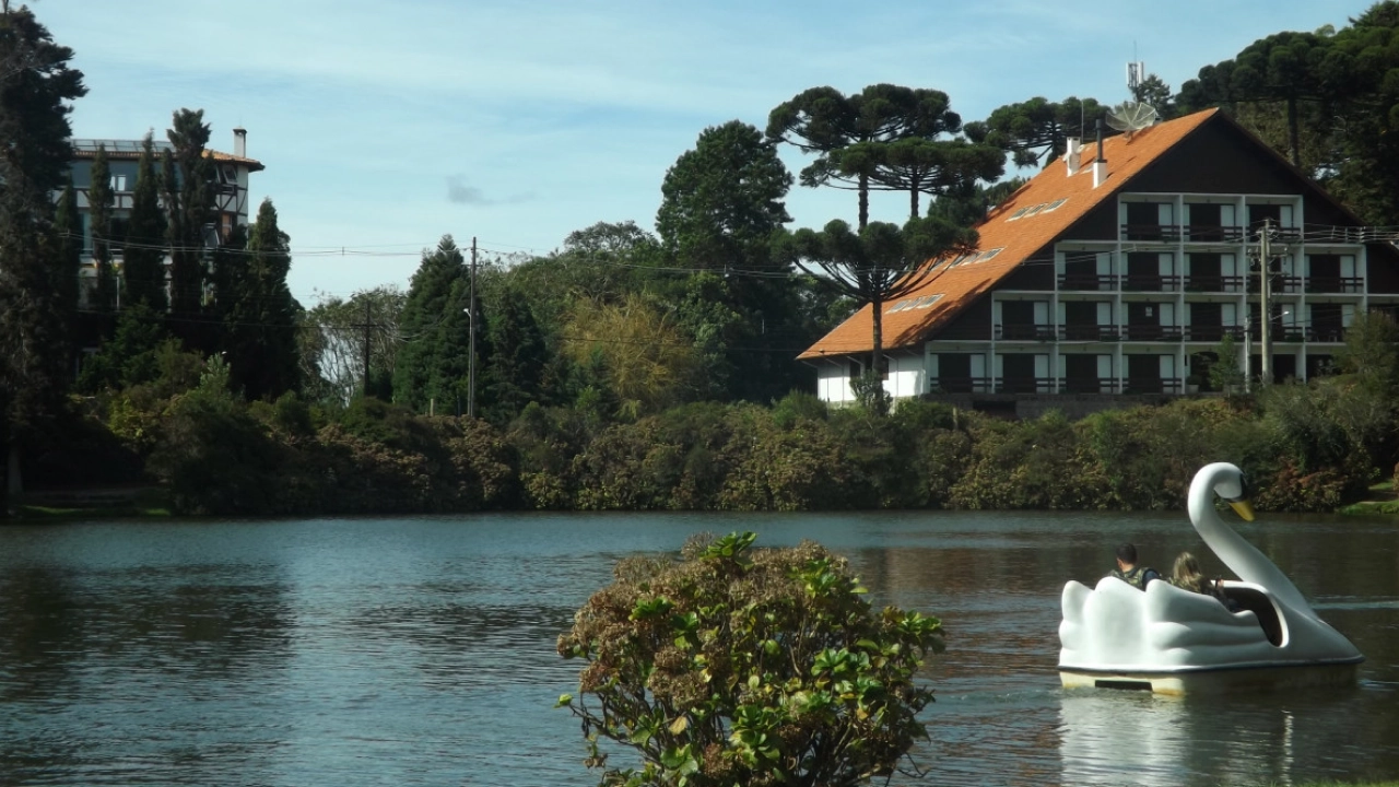 O Lago Negro em Gramado, Rio Grande do Sul, com pedalinhos em formato de cisne, rodeado por árvores e um charmoso hotel de arquitetura europeia ao fundo.