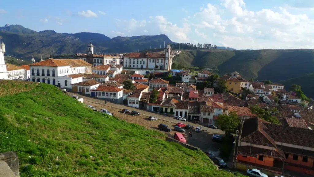 Vista panorâmica de uma cidade histórica em Minas Gerais, com construções coloniais, igrejas antigas e montanhas ao fundo.