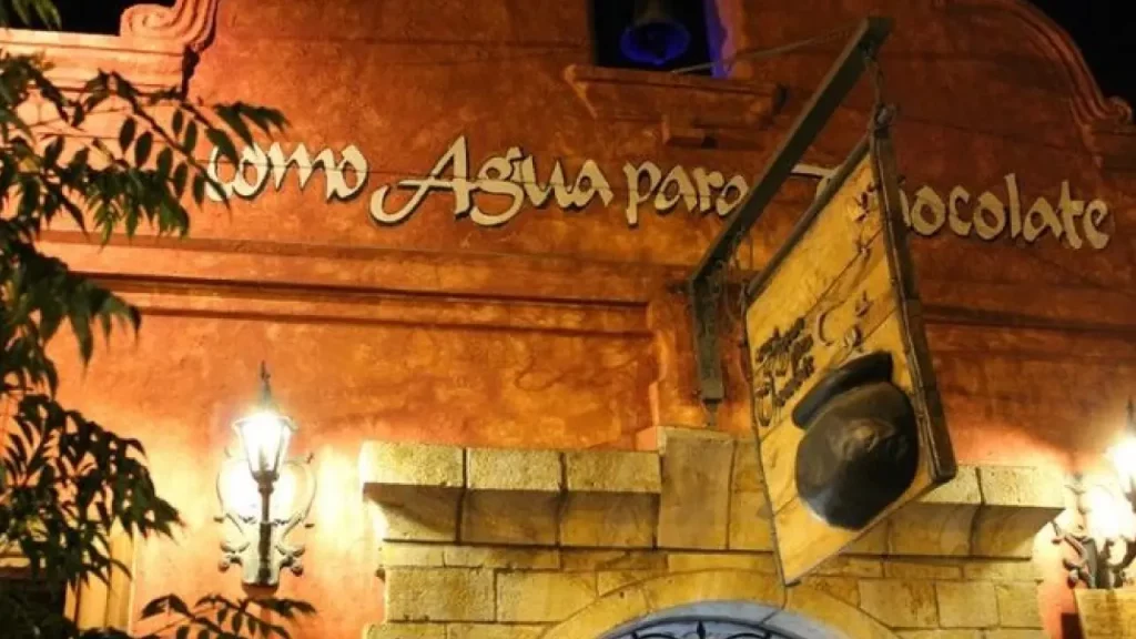 Fachada do restaurante Como Agua Para Chocolate em Santiago, com letreiro iluminado e estilo arquitetônico colonial em tons terrosos.