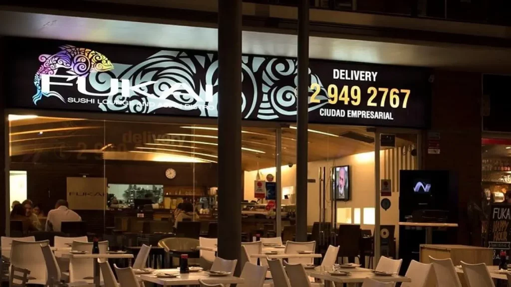 Fachada do restaurante Fukai Sushi Lounge na Ciudad Empresarial, com ambiente moderno, mesas ao ar livre e letreiro iluminado.
