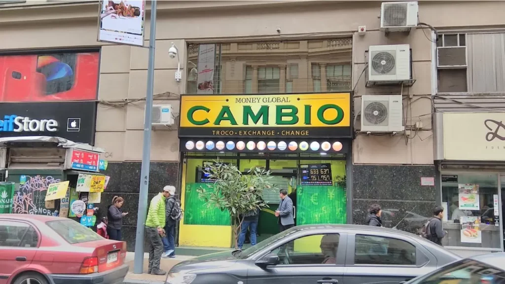 Vista da casa de câmbio Money Global em Santiago, Chile, com letreiro amarelo e verde e cotações visíveis na entrada.