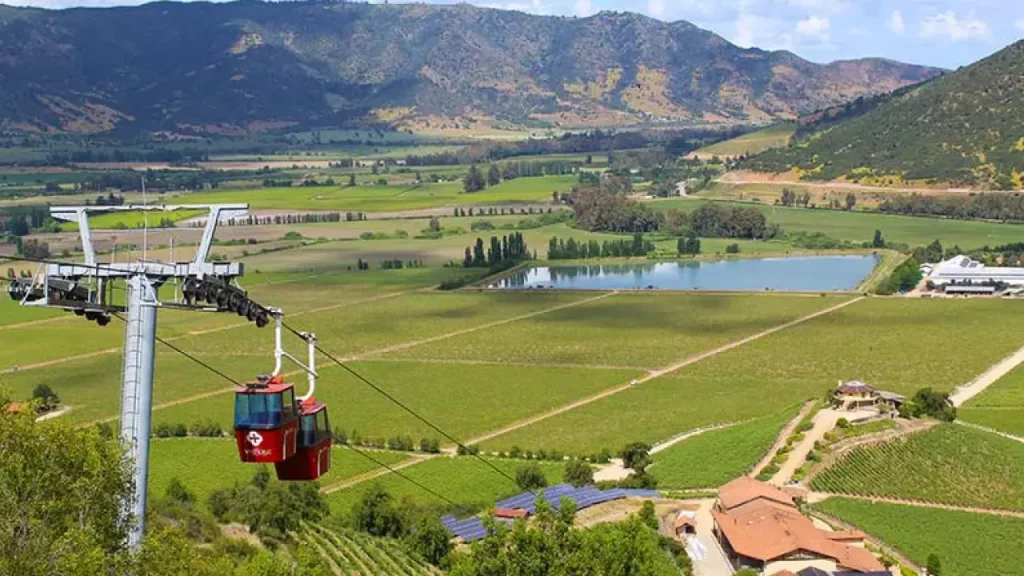 Vinhedos no Valle de Colchagua, Chile, com teleférico vermelho passando sobre as plantações e montanhas ao fundo.