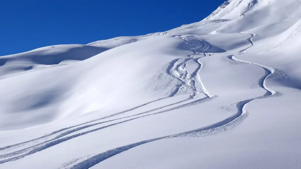 Montanha coberta por neve virgem com marcas de esqui sob céu azul claro, cenário típico dos Andes chilenos no inverno.
