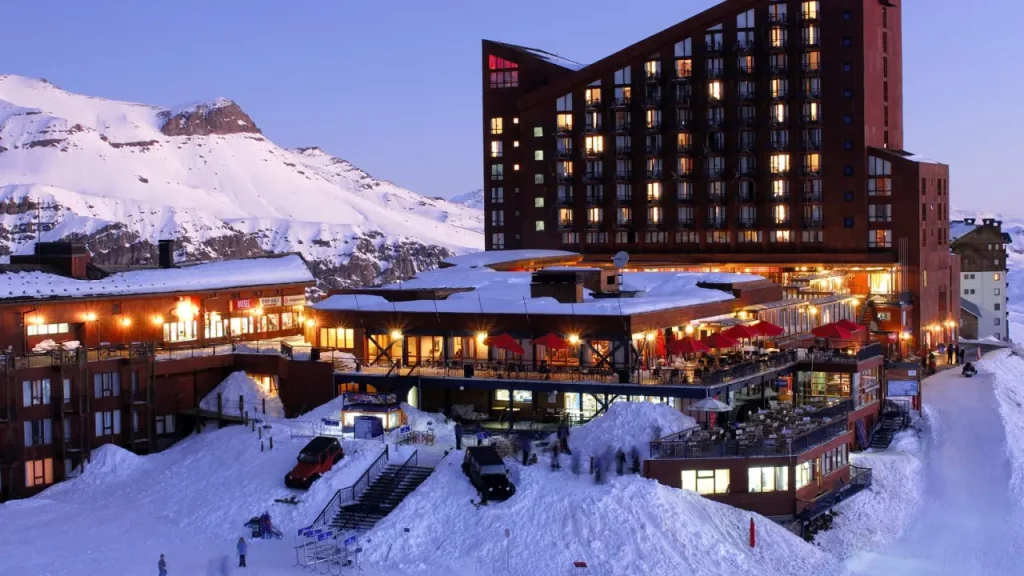 Resort de esqui Valle Nevado no Chile ao entardecer, com montanhas cobertas de neve e iluminação aconchegante.