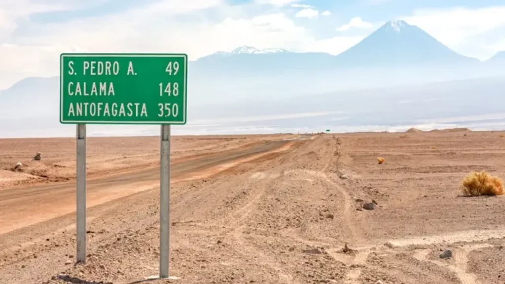 Placa de estrada no Deserto do Atacama indicando as distâncias para San Pedro de Atacama, Calama e Antofagasta, com montanhas ao fundo.