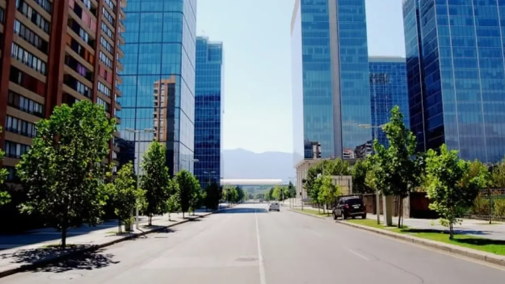Avenida moderna e arborizada em Las Condes, Santiago, com prédios comerciais de vidro espelhado e vista para as montanhas ao fundo.