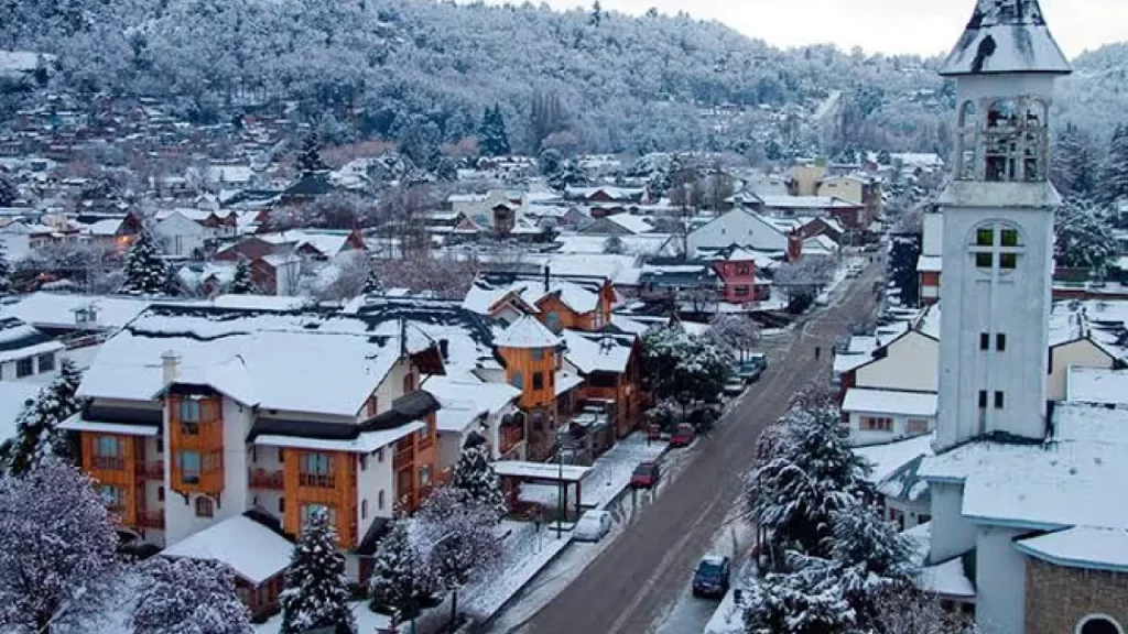 Cidade coberta de neve com casas de estilo alpino e montanhas ao fundo em San Martín de los Andes.