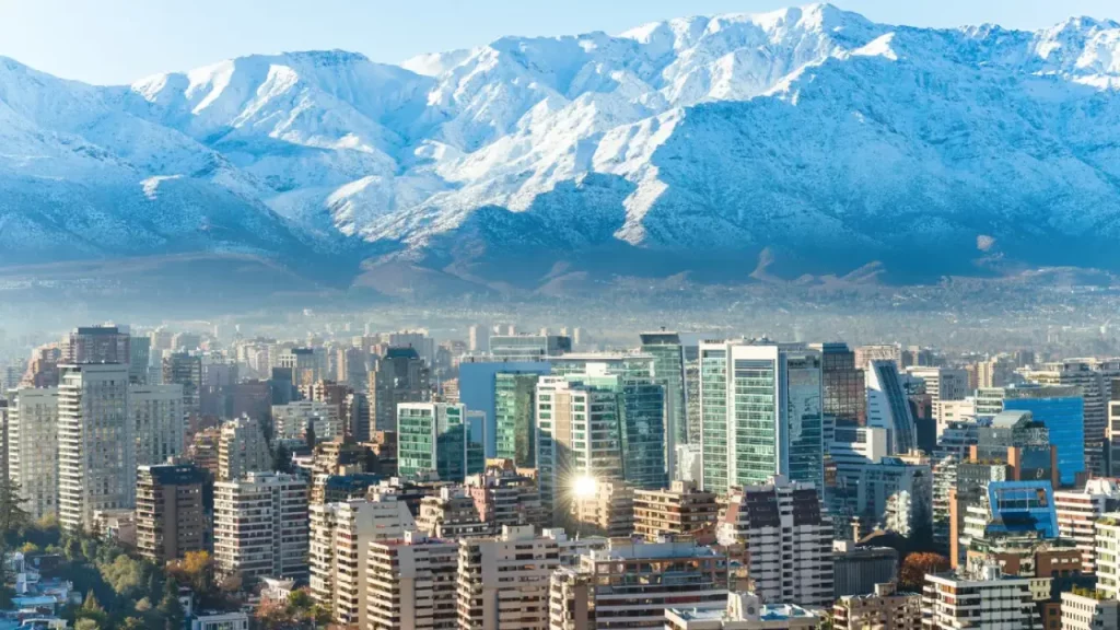 Vista panorâmica de Santiago do Chile com prédios modernos e a Cordilheira dos Andes coberta de neve ao fundo.