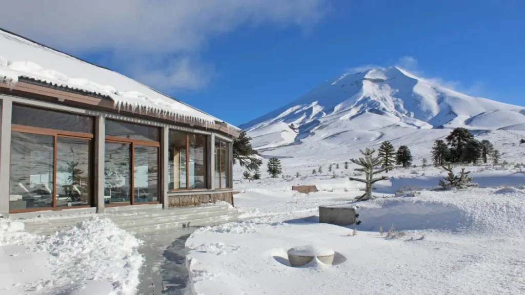 Vista externa do Corralco Resort com o Vulcão Lonquimay ao fundo coberto de neve, em meio à Reserva Nacional Malalcahuello, Chile.