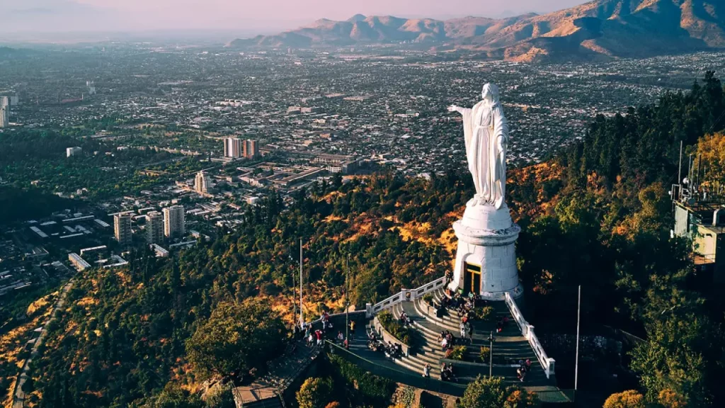 Vista aérea da estátua da Virgem Imaculada no topo do Cerro San Cristóbal, com a cidade de Santiago ao fundo e visitantes no mirante.