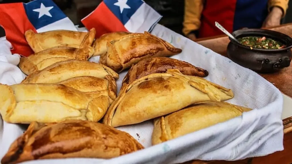 Uma cesta de empanadas chilenas douradas, decorada com pequenas bandeiras do Chile, pronta para ser servida.