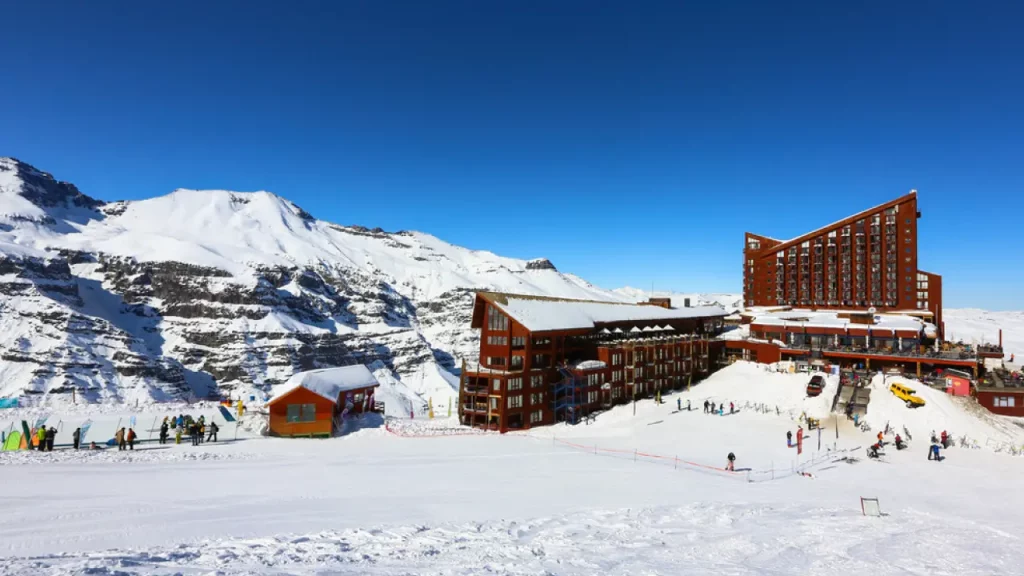 Vista do complexo hoteleiro de Valle Nevado em um dia de sol, com pistas de esqui e montanhas cobertas de neve ao redor.