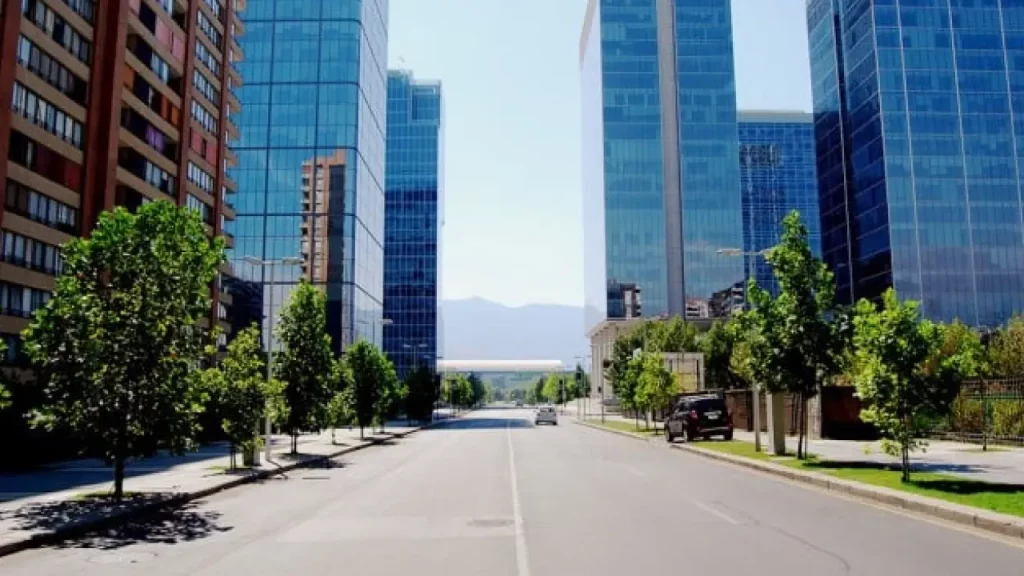 Avenida tranquila cercada por prédios espelhados no bairro de Las Condes, em Santiago, com a Cordilheira dos Andes ao fundo.