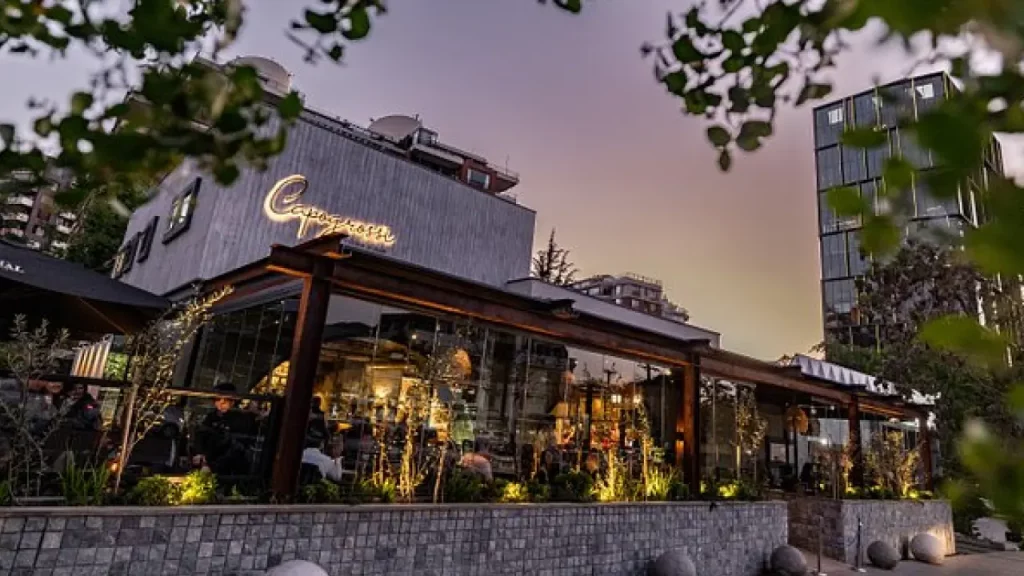 Restaurante moderno e iluminado ao entardecer em bairro nobre de Santiago, com fachada de vidro e clima aconchegante.