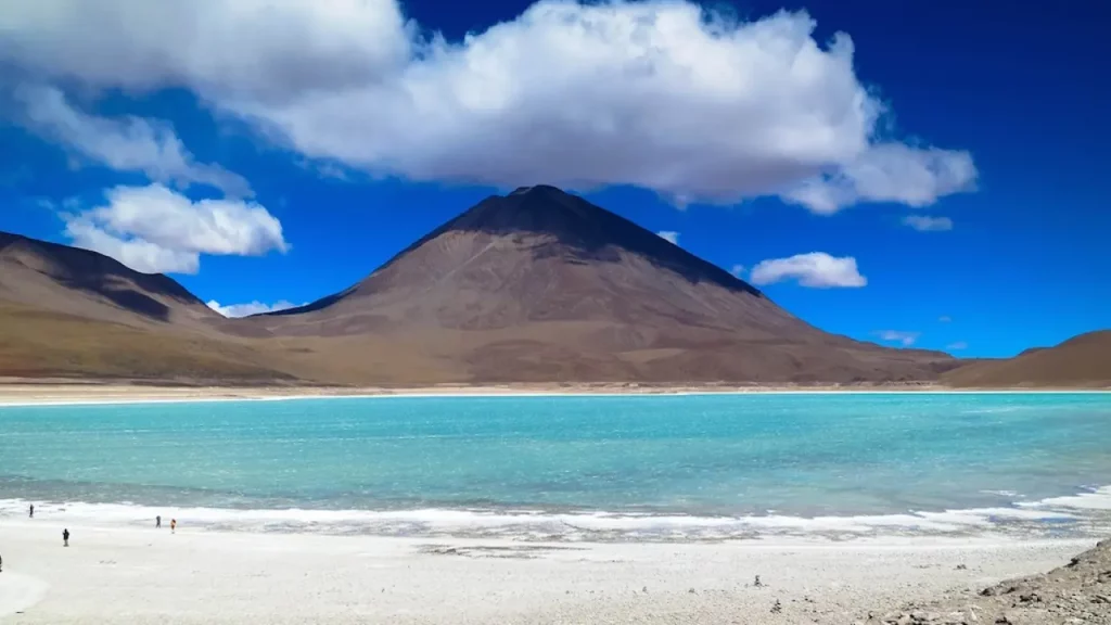 Laguna Verde no Deserto do Atacama com água azul-turquesa, salinas brancas e montanha escura ao fundo, sob céu azul intenso.